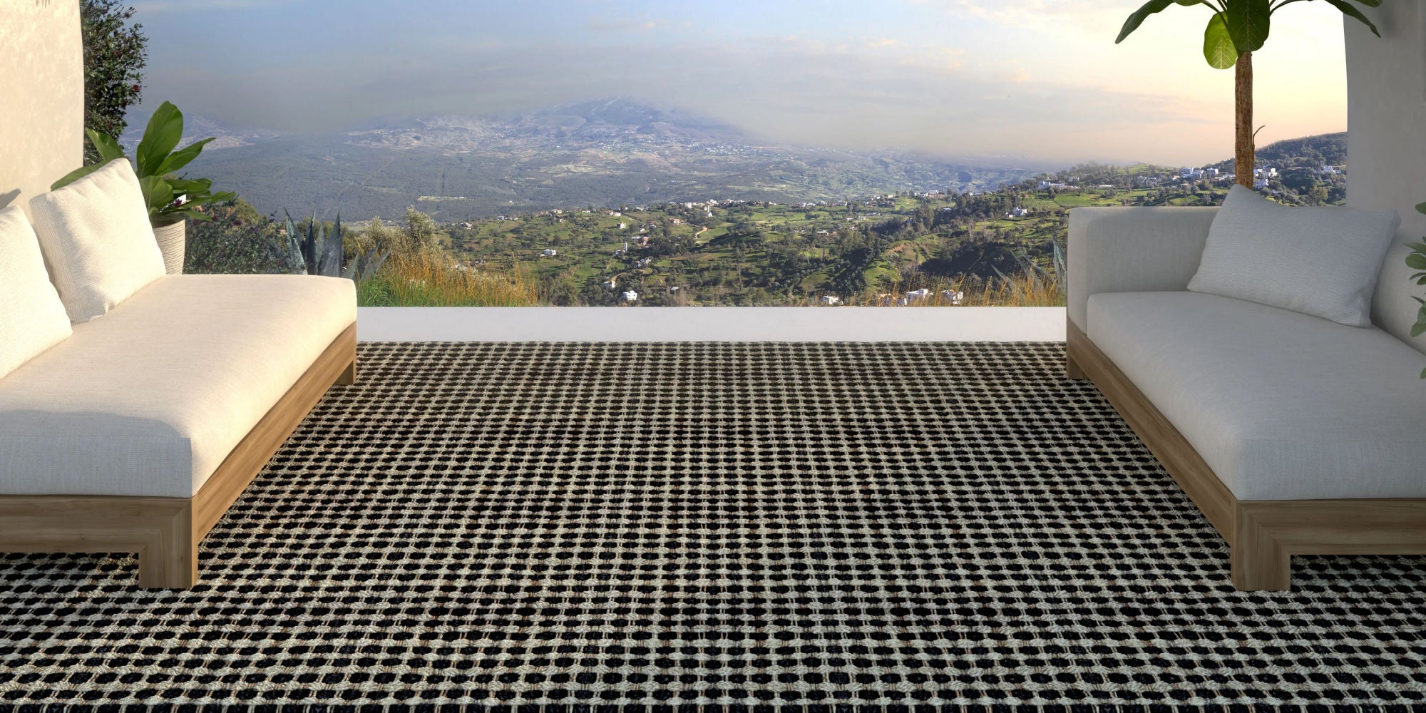Outdoor patio with checkered rug, white cushioned chairs, and scenic view.